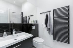 A black and white modern bathroom features a large heated towel rack mounted to the wall.