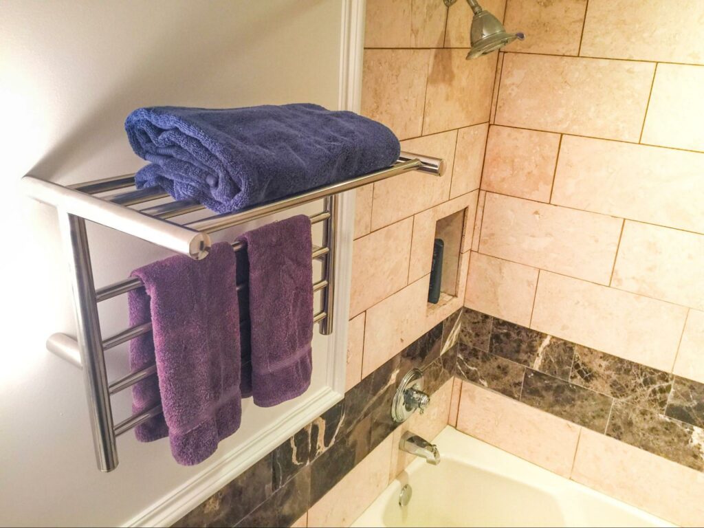 A silver heated towel rack in a bathroom with blue and purple towels.