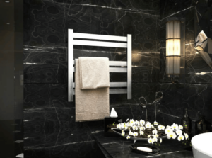 A silver finished heated towel rack mounted on a black marbled bathroom wall.