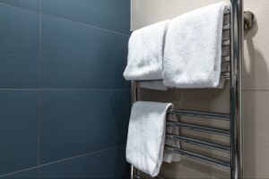 A heated towel rack is mounted on a bathroom wall with three hand towels draped over the bars.
