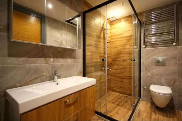 A contemporary cabin bathroom with wooden details and a heated towel rack above the toilet.
