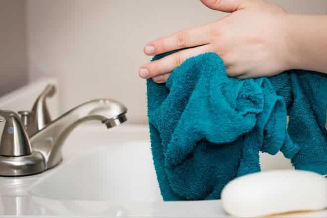 A light-skinned individual dries their hands with a turquoise towel.