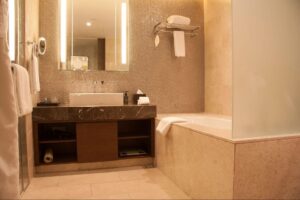 A warm toned guest bathroom with a bathtub, heated towel rack, and lighted mirror.