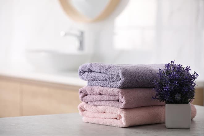 A stack of three pink and purple towels beside a potted purple flower.