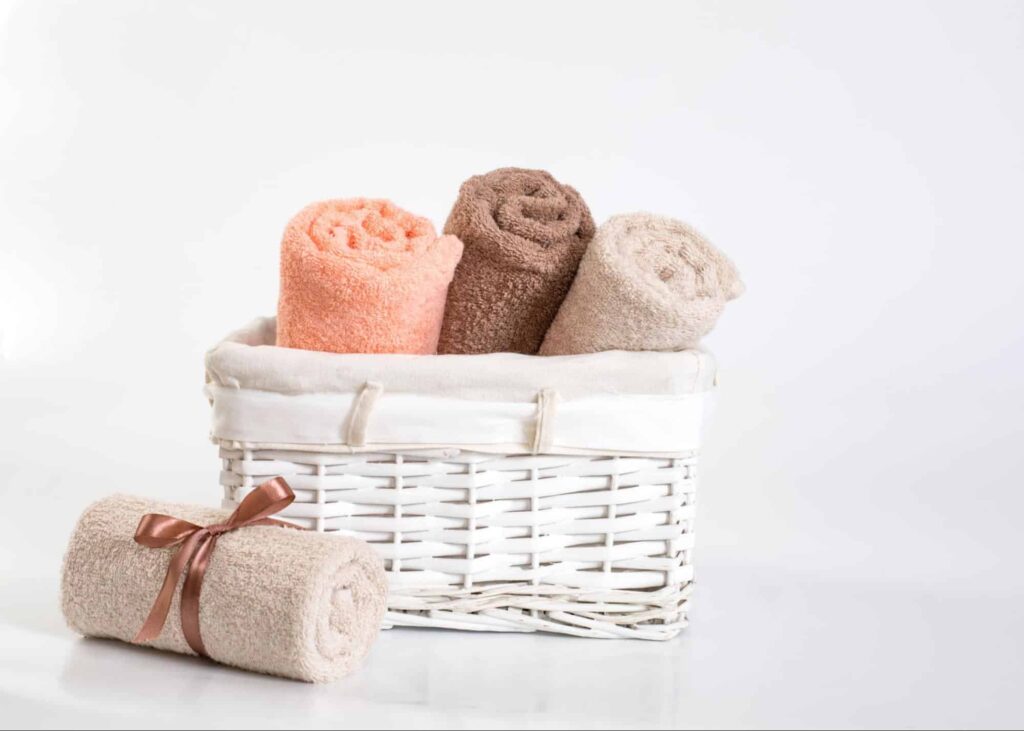 Three rolled towels in a white basket with another rolled towel, tied with ribbon, resting beside it.