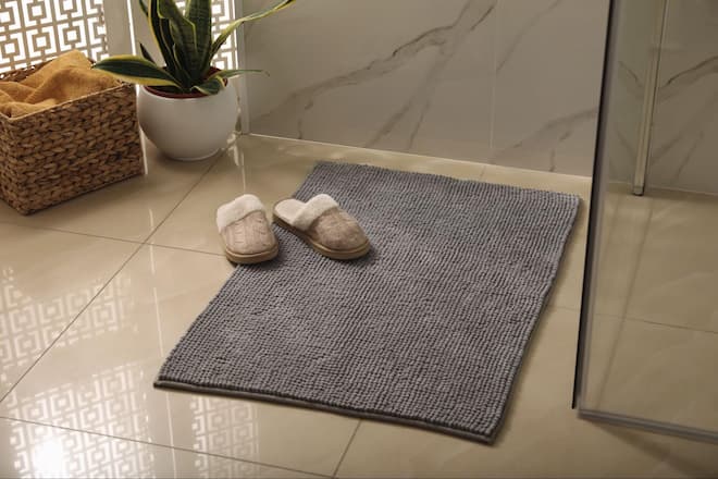 A washed memory foam bath mat with slippers outside a standing shower.