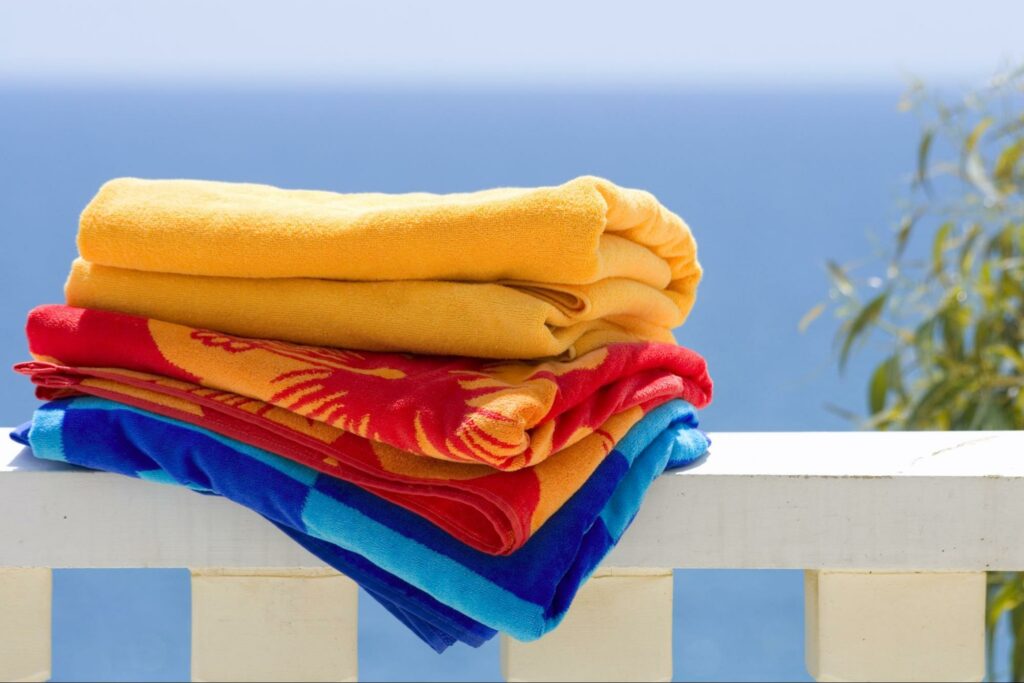 A stack of three folded colorful beach towels sitting on a white railing outside.