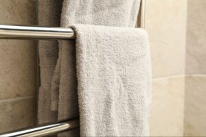 Gray towels hanging on a heated towel rack in a bathroom with beige tiles.