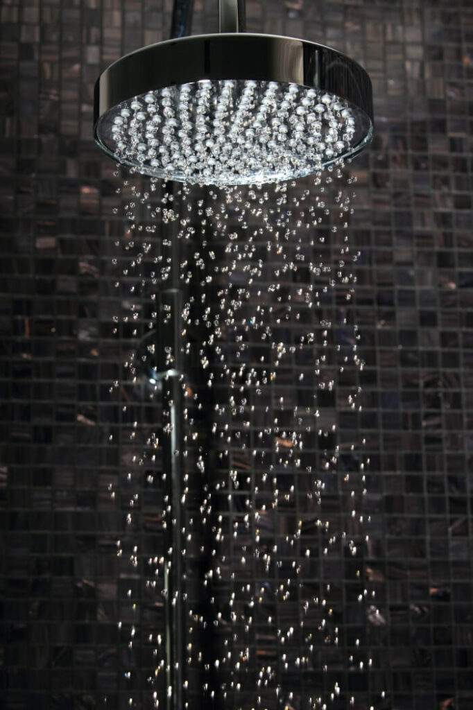 A luxurious rainfall shower head against a black tile shower.